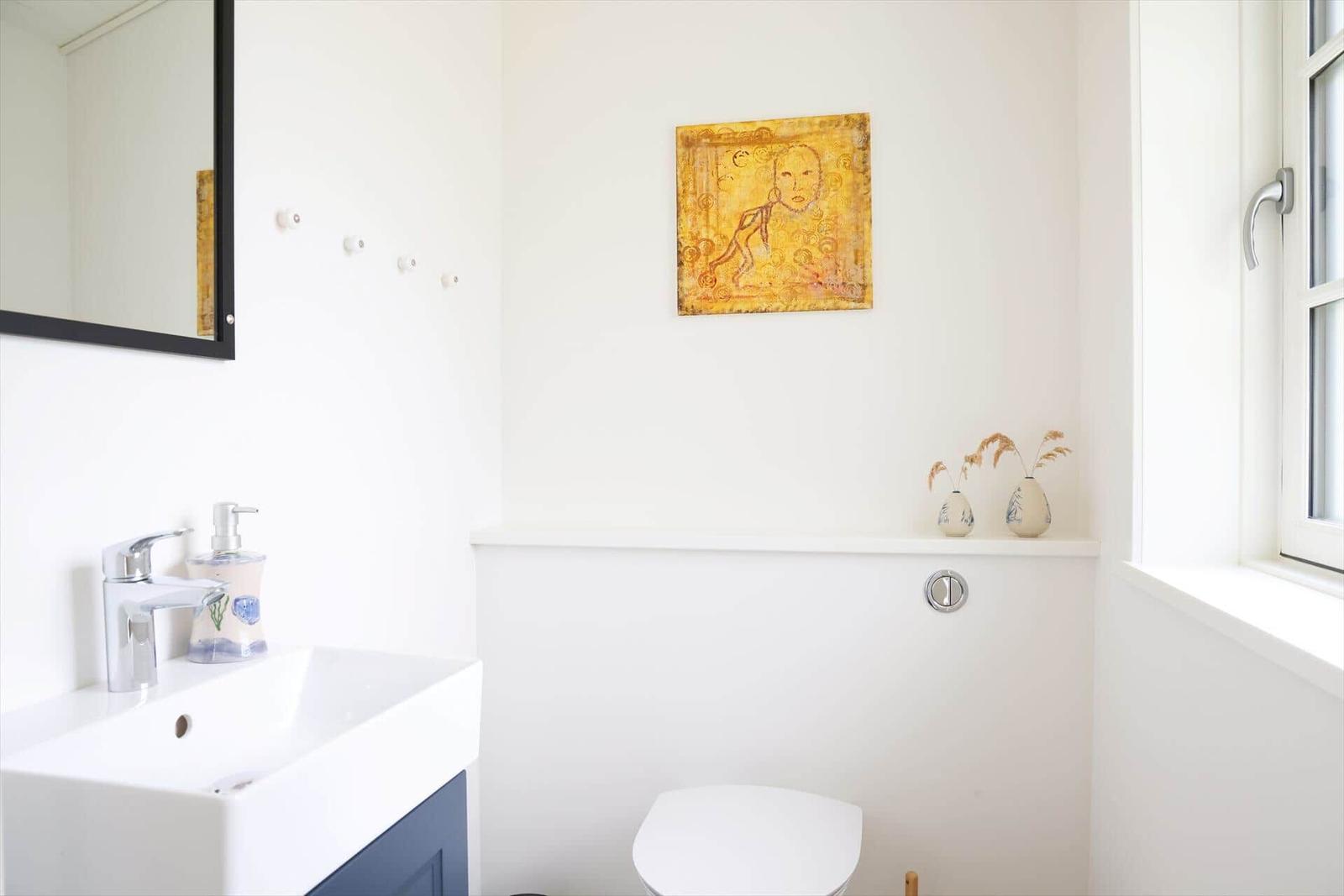 Badezimmer mit Waschbecken, Spiegel, Toilette und Fenster.