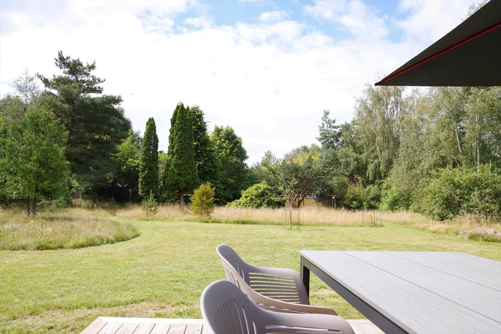 Terrasse mit Tisch und Stühlen, Blick auf grünen Rasen und Bäume.