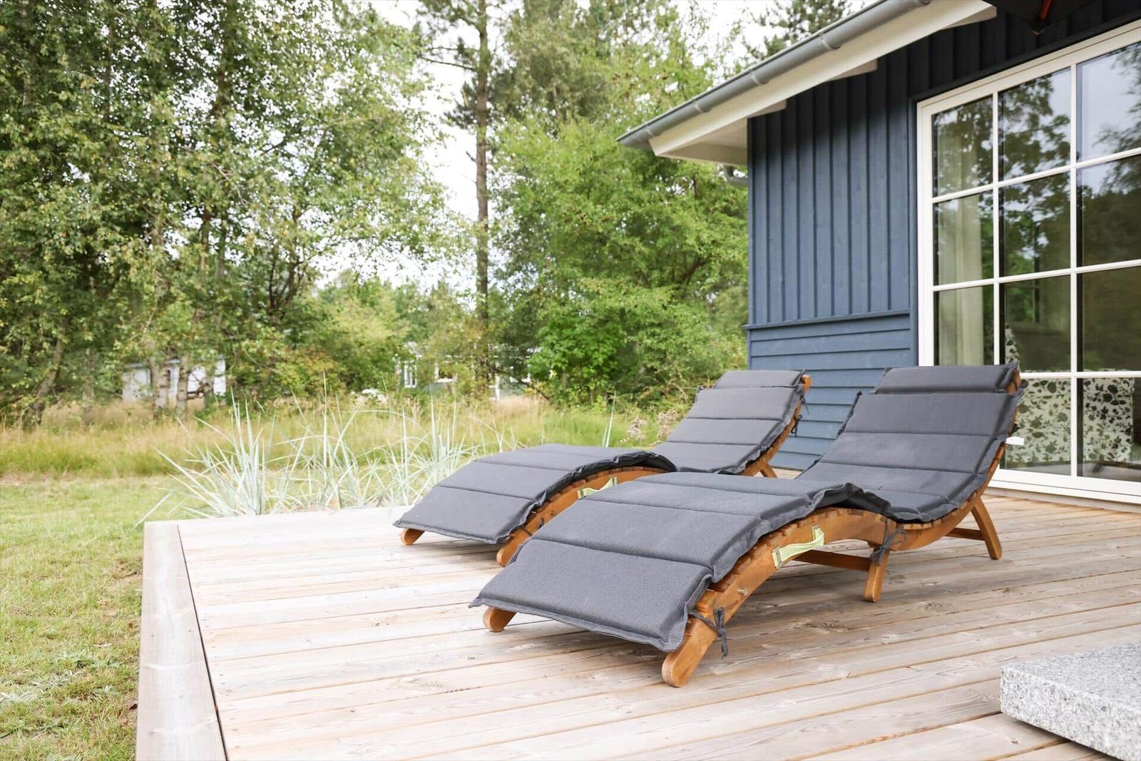 Zwei Liegestühle mit Kissen auf einer Holterrasse vor einem Haus mit blauen Wänden.