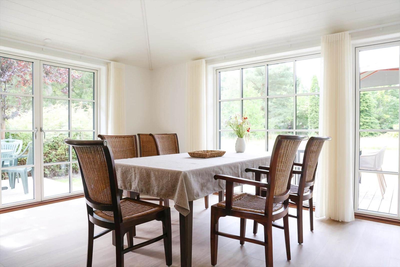 Esszimmer mit Tisch, Stühlen und großen Fenstern zur Außenterrasse.