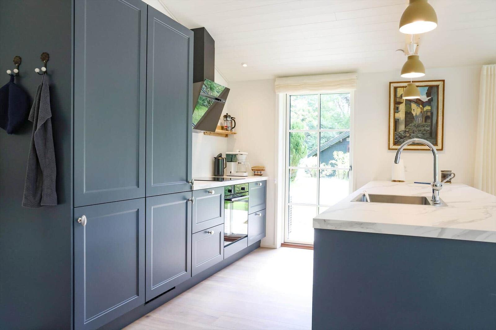 Küche mit blauen Schränken, Marmorarbeitsplatte und Fenster zum Garten.