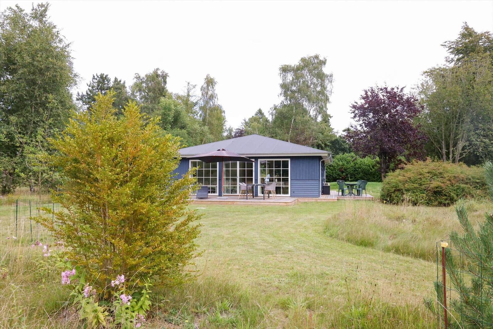 Ein blau gestrichenes Haus mit Terrasse und Garten. Außentisch mit Sonnenschirm.