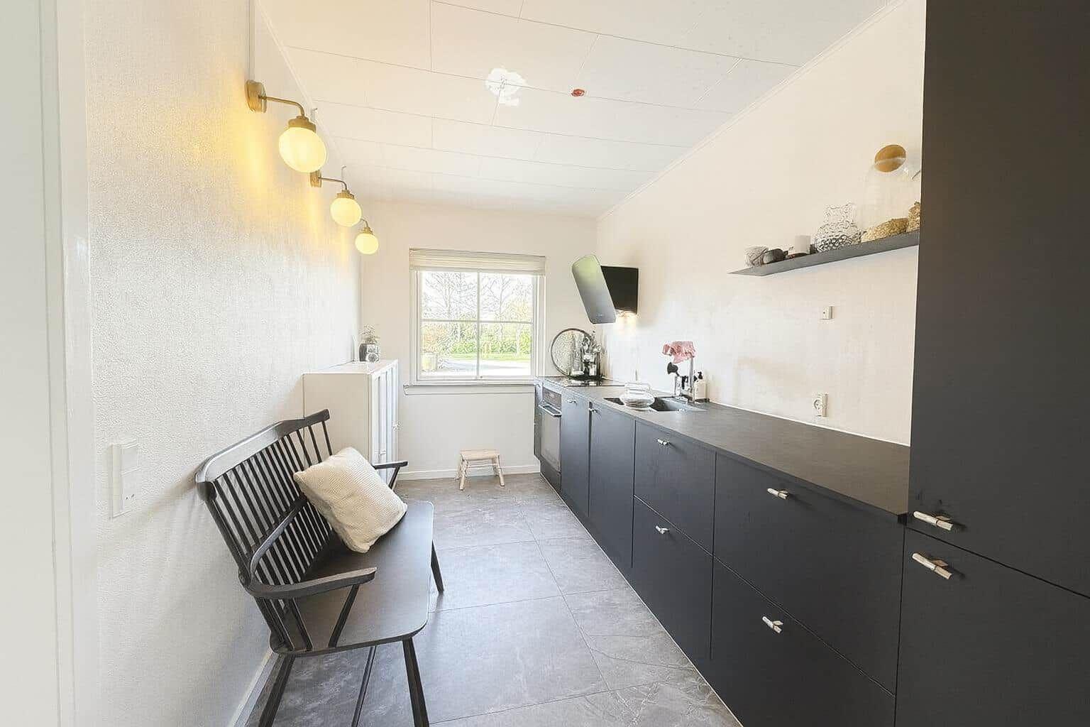 Küche mit dunklen Schränken, Fenster und Bank mit Kissen.