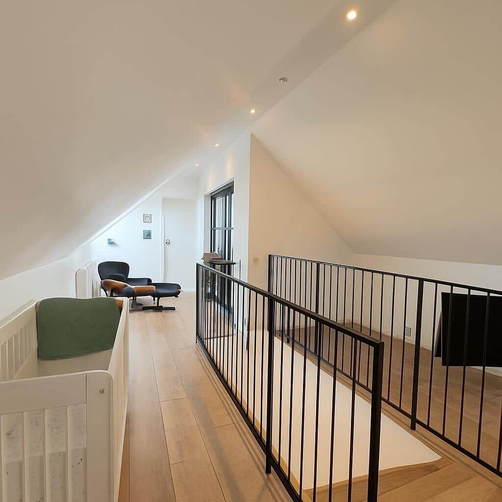 Dachgeschoss mit Holzboden, schwarzer Metallbrüstung und Babybett.