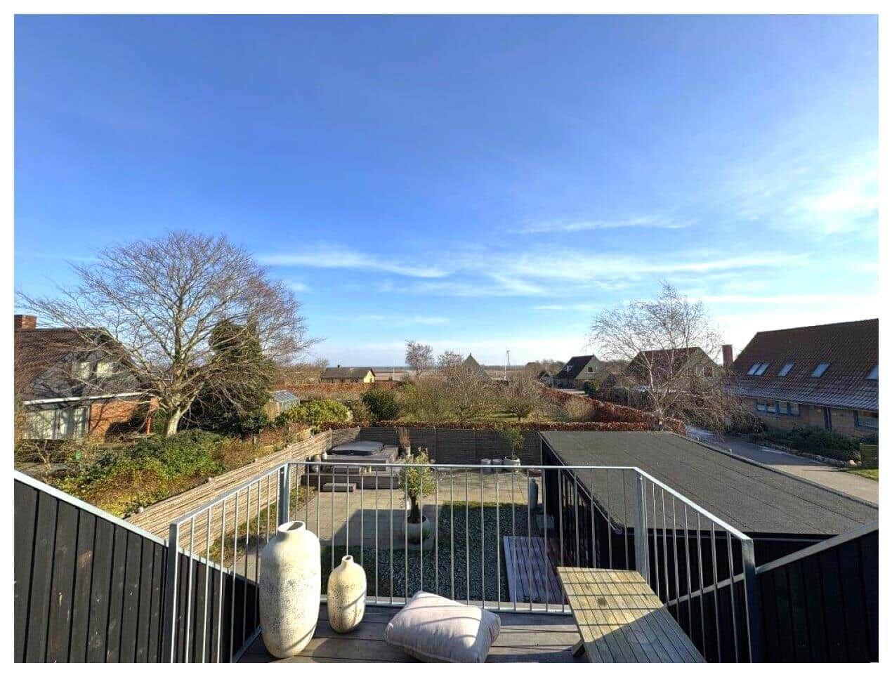 Terrasse mit Blick auf Garten und Nachbarhäuser unter blauem Himmel.