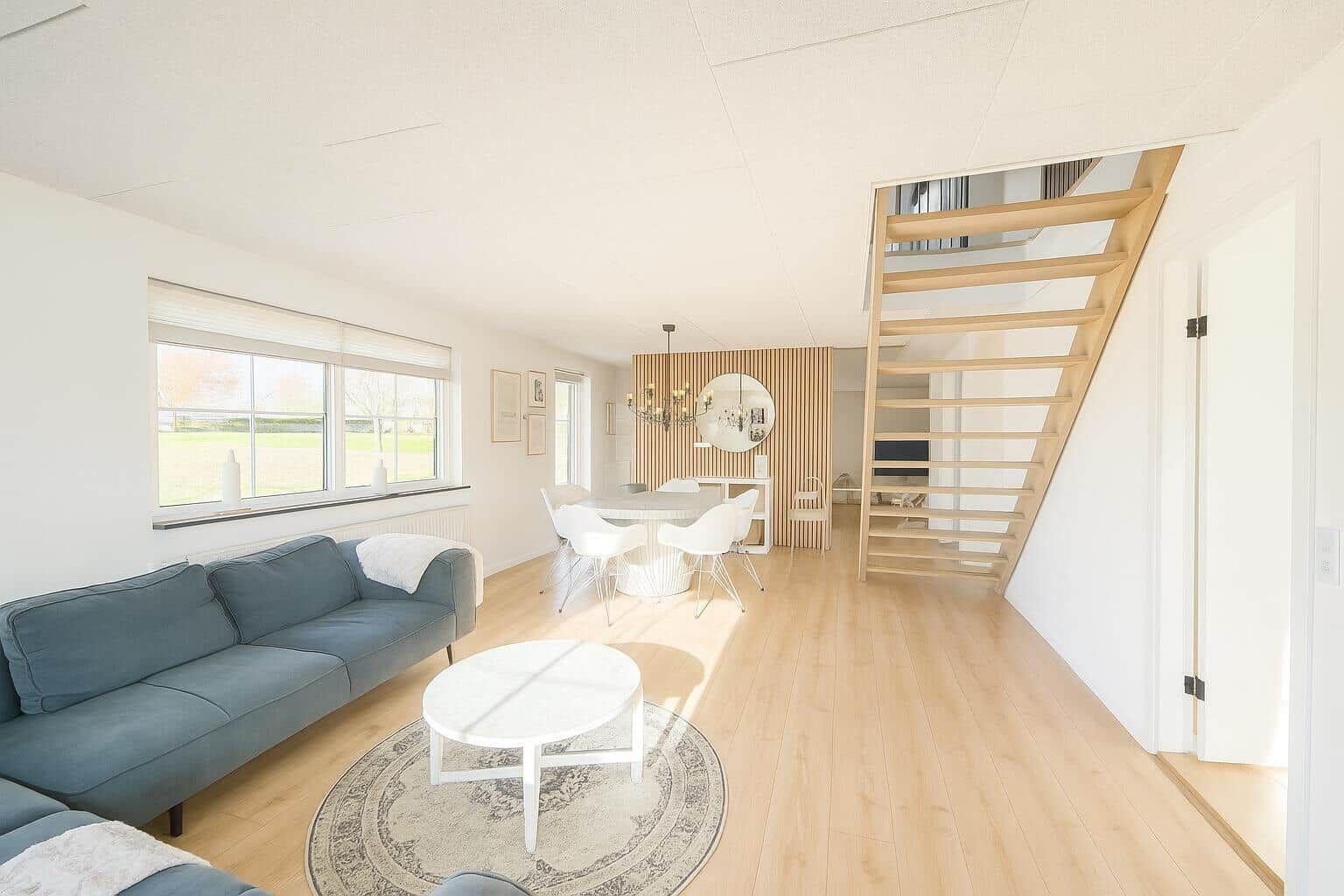 Wohn- und Essbereich mit Holzboden, Sofa und Treppe zur oberen Etage.