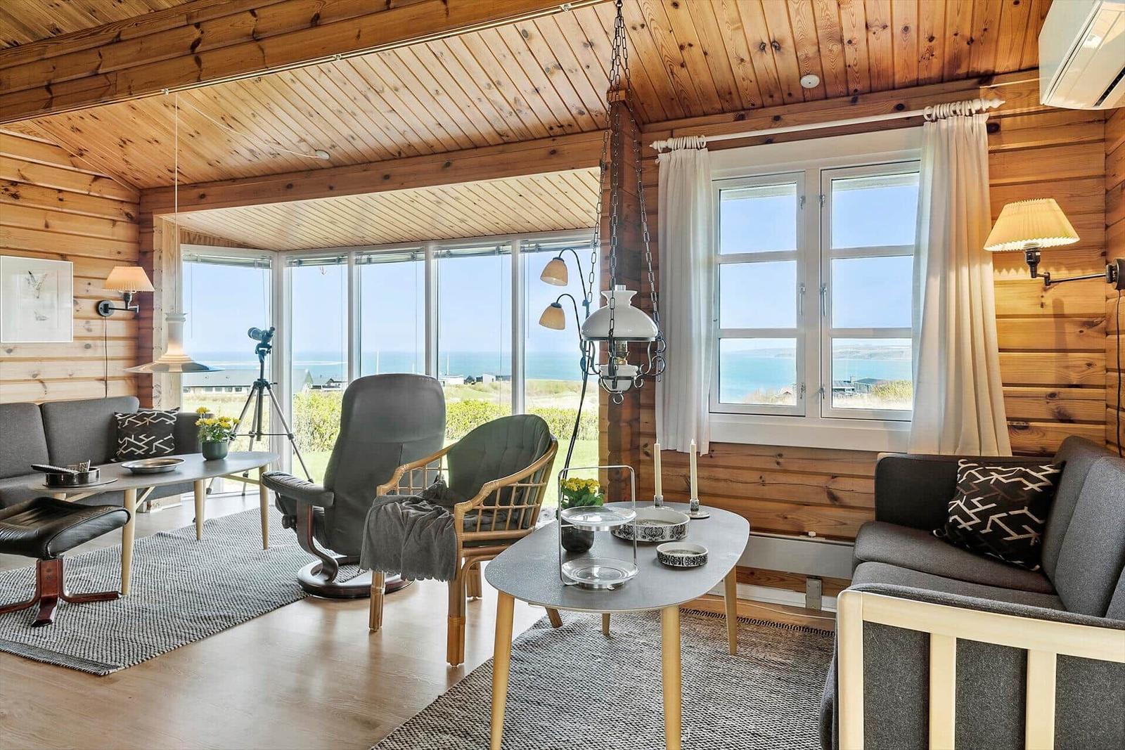 Wohnzimmer mit Holzwänden, großen Fenstern und Meerblick.