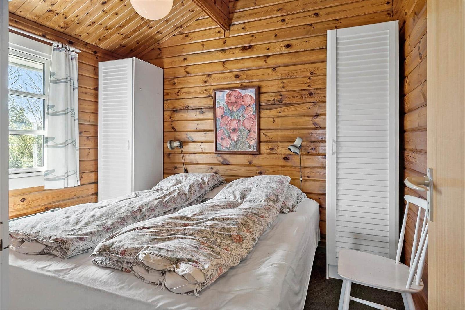 Schlafzimmer mit Holzwand, Bett, Kleiderschrank und Stuhl.