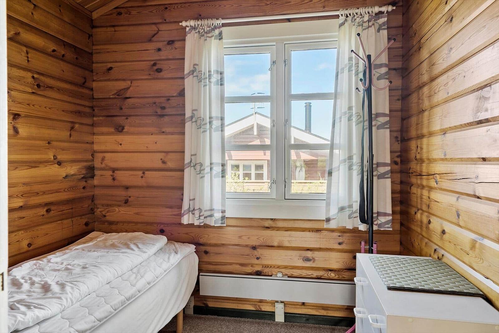 Schlafzimmer mit Holzwand, Bett, Fenster und Kleiderständer.