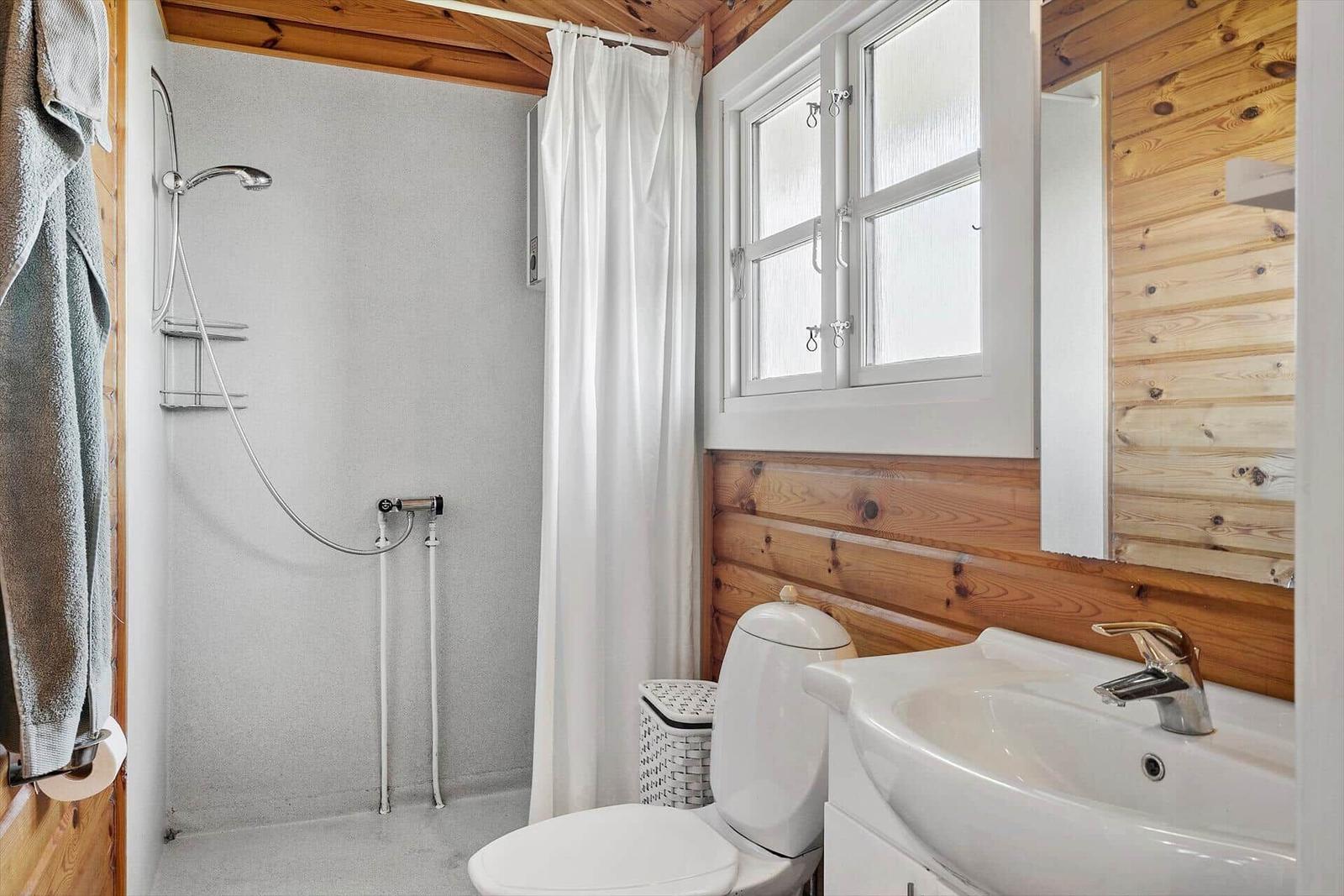 Badezimmer mit Dusche, Toilette und Waschbecken. Holzwände und Fenster.