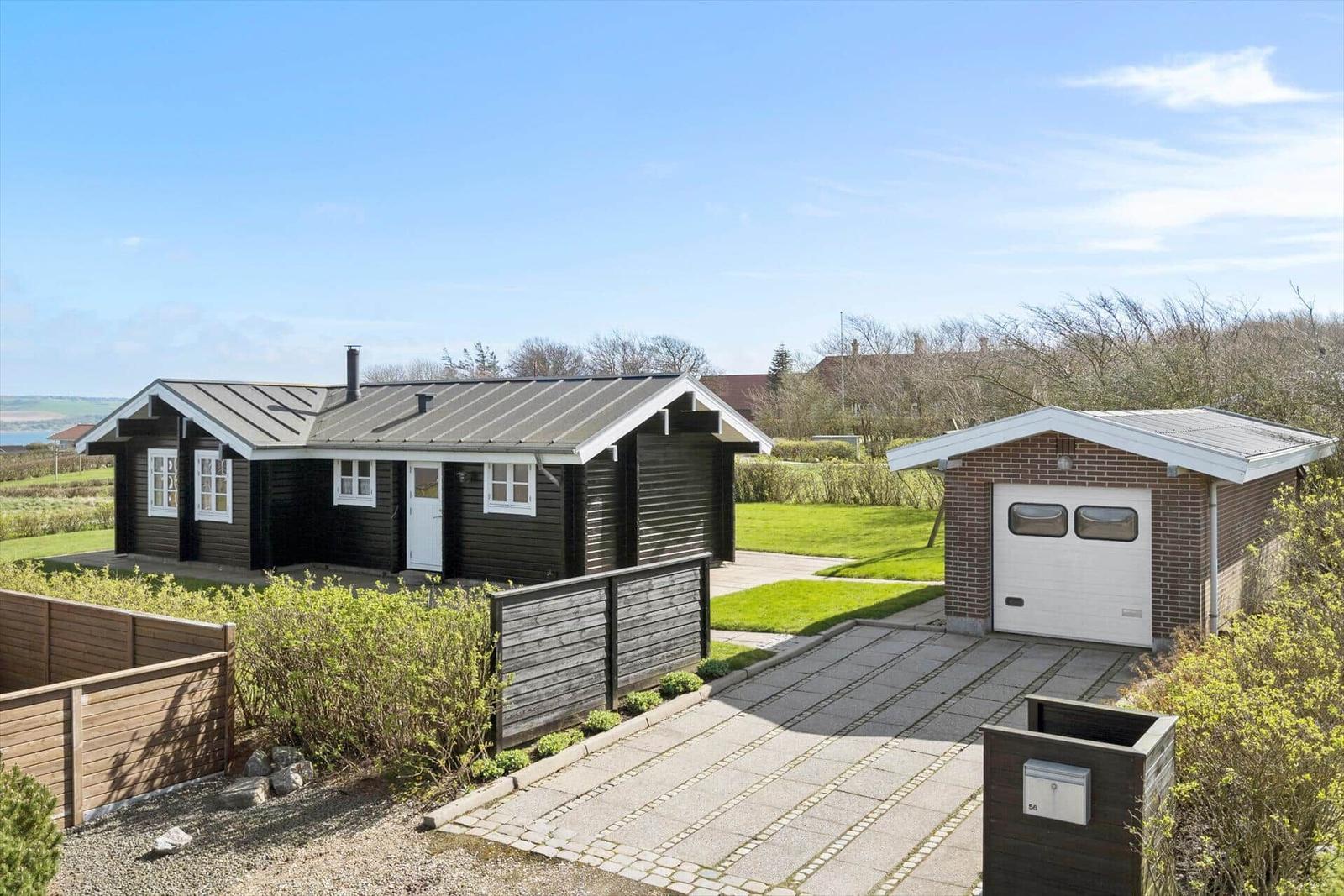 Holzhaus mit Garage und gepflastertem Weg. Grünflächen und Zaun sichtbar.