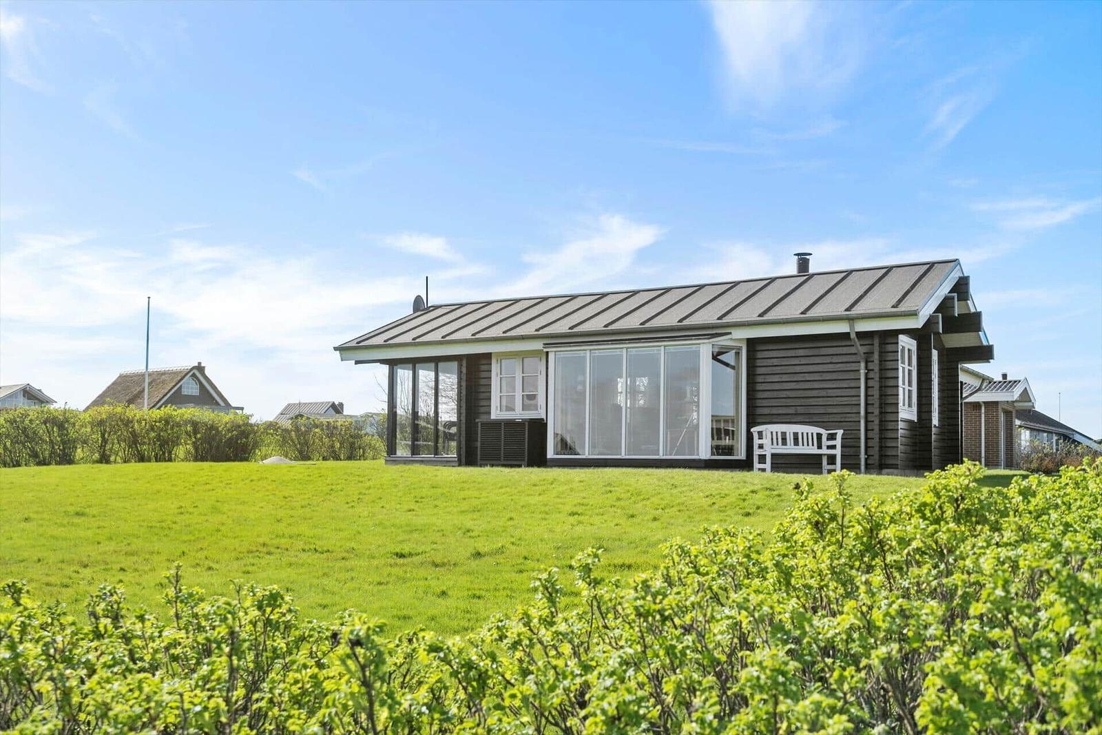 Ein Haus mit dunklem Holz und großen Fenstern steht auf einer grünen Wiese.