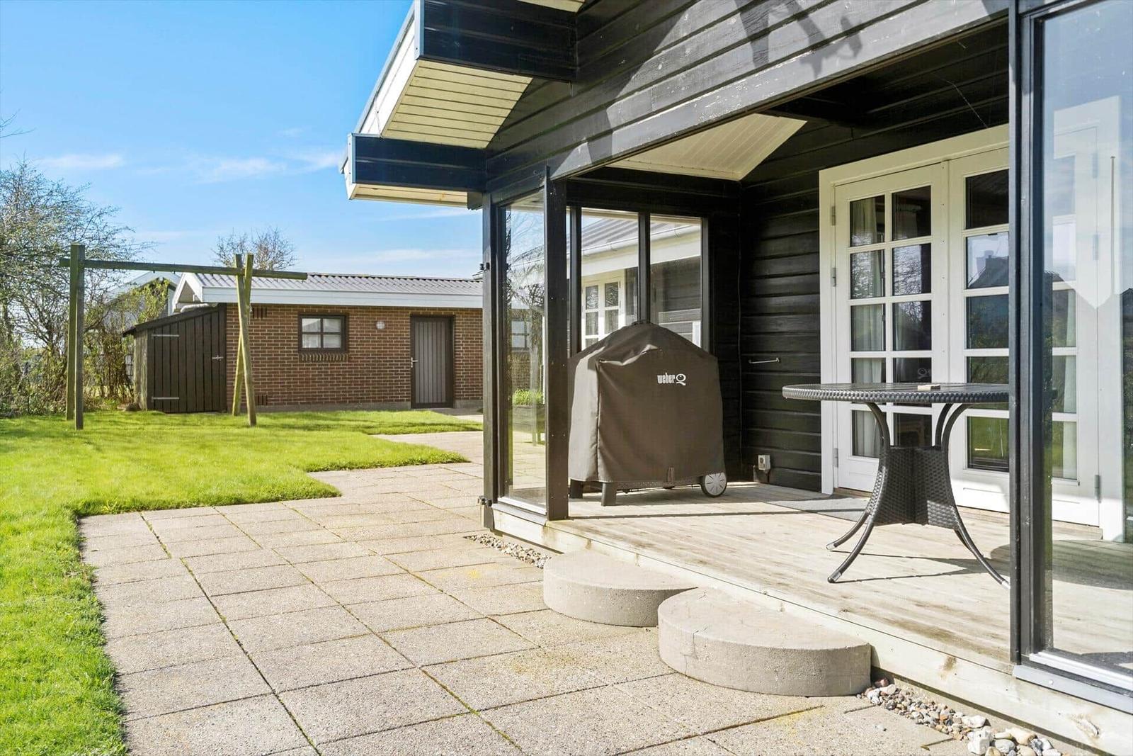 Terrasse mit Grill und Tisch. Hinterhof mit Rasen und Steinweg.