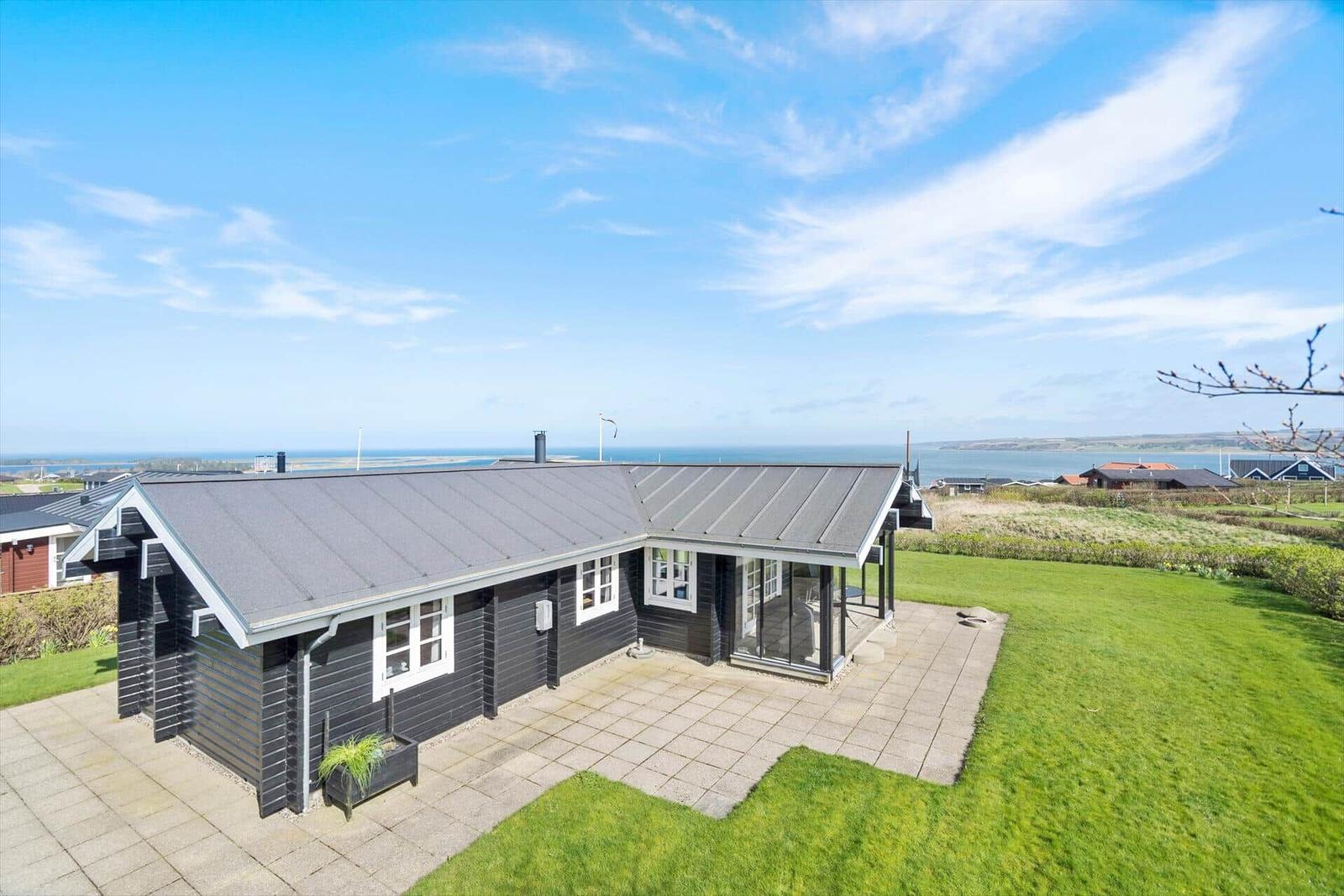 Schwarzes Holzhaus mit Terrasse und Blick aufs Meer.