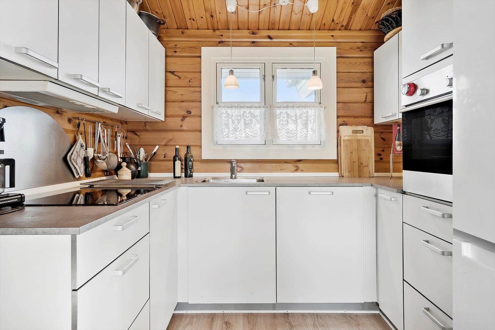 Küche mit weißen Schränken, Holzwand und Fenster mit Vorhang.