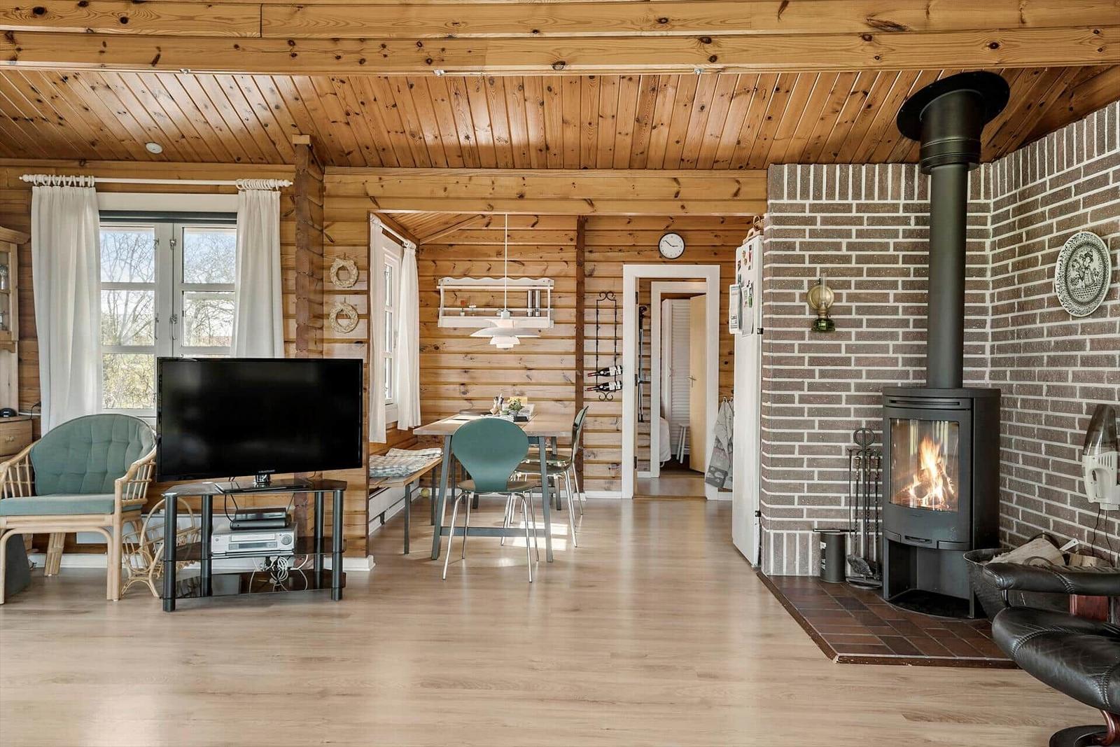 Wohn- und Essbereich mit Kamin, TV und Holzdecke.