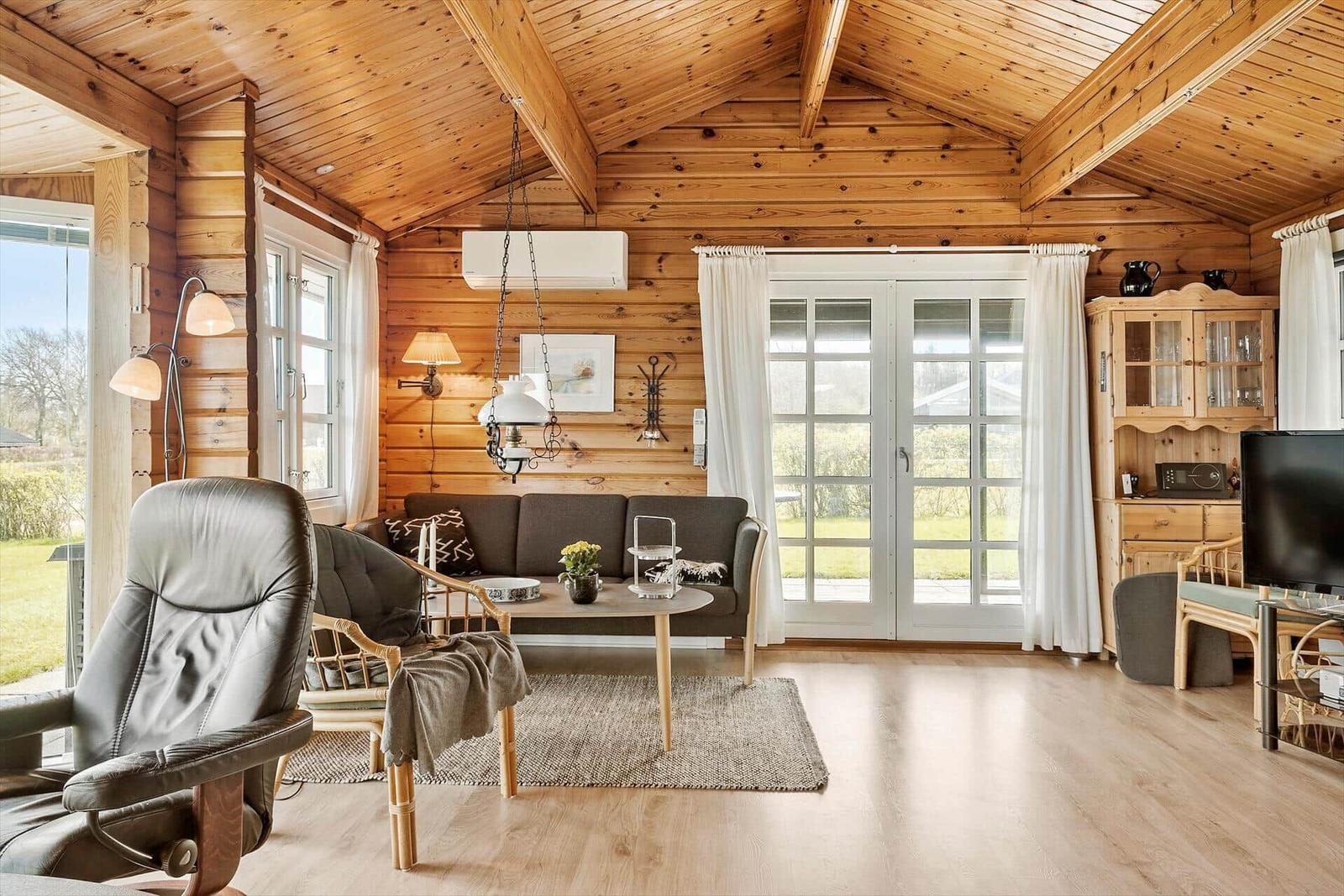 Wohnzimmer mit Holzdecke, Sofa, Sessel und Fernseher.