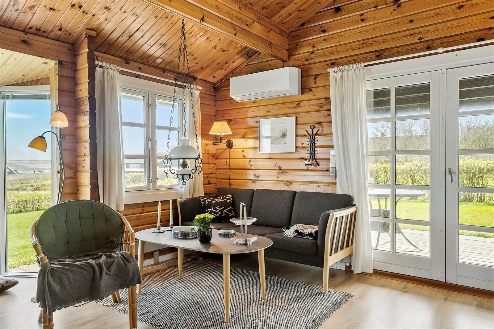 Wohnzimmer mit Holzwand, Sofa, Stuhl und Tisch. Fenster und Tür zur Terrasse.