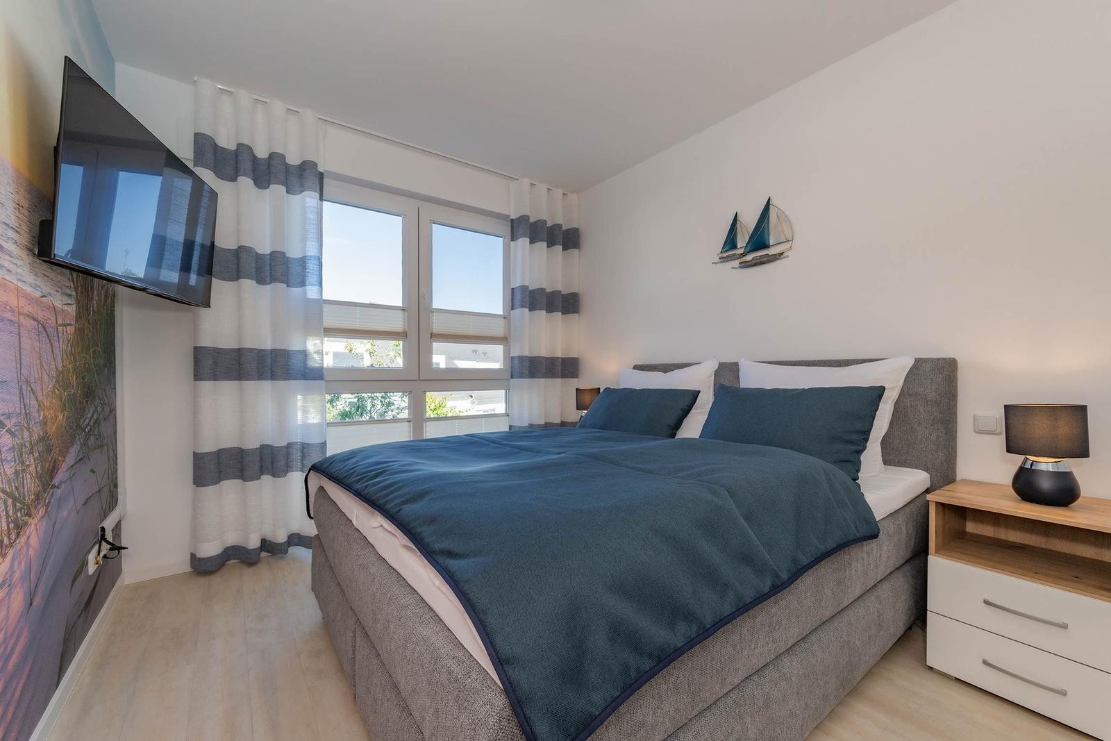 Schlafzimmer mit Bett, TV und Fenster mit Vorhängen.