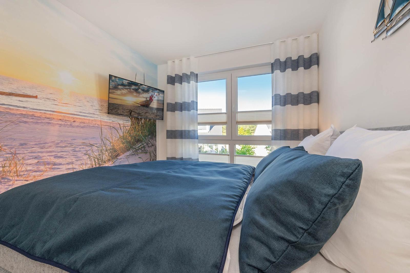 Schlafzimmer mit Bett, Fenster und Strandmotiv an der Wand.