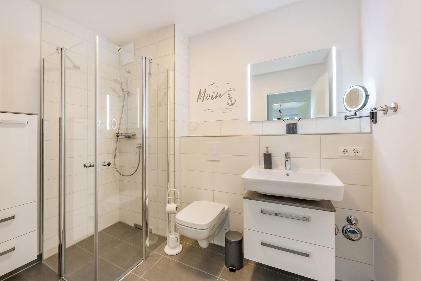 Badezimmer mit Dusche, Waschbecken und Toilette. Wanddekoration mit Ankermotiv.