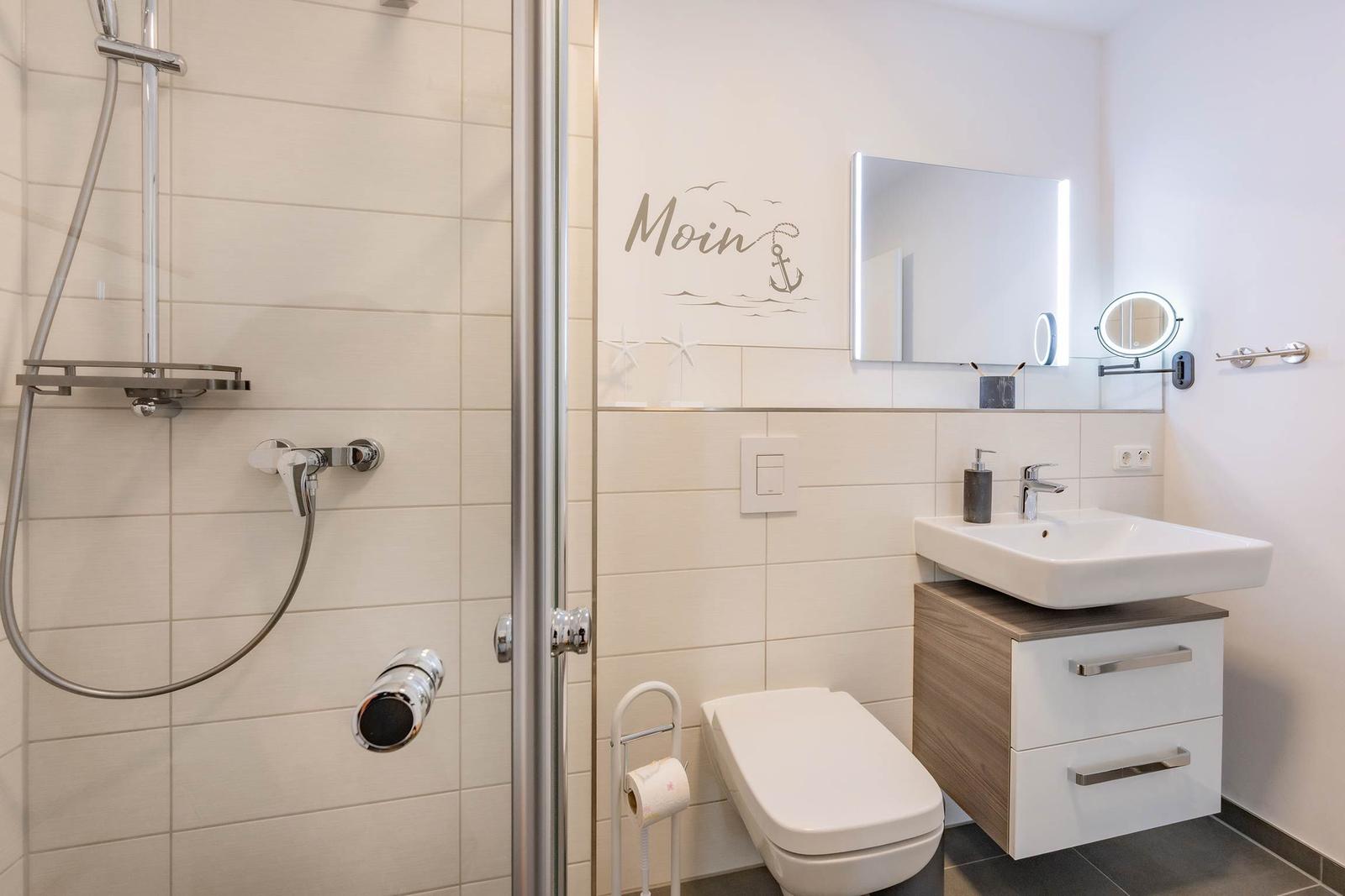 Badezimmer mit Dusche, Waschbecken und Toilette. Wanddekoration mit Anker-Motiv.