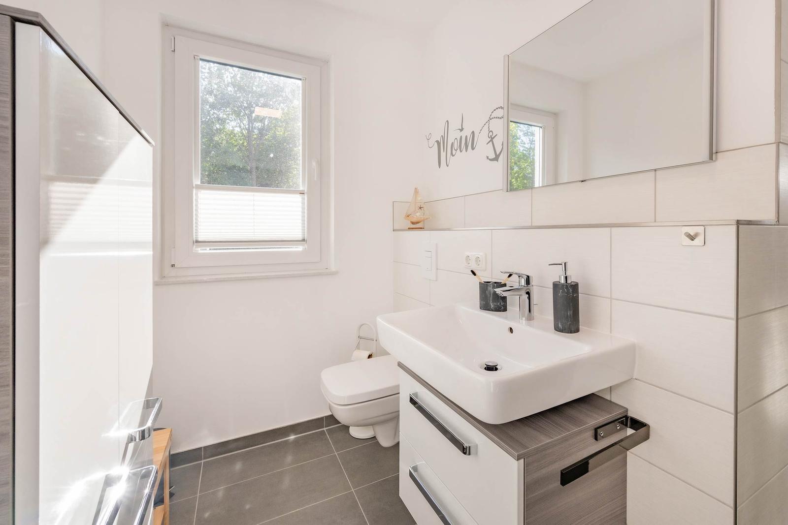 Badezimmer mit Waschbecken, Toilette und Dusche. Fenster mit Jalousie.