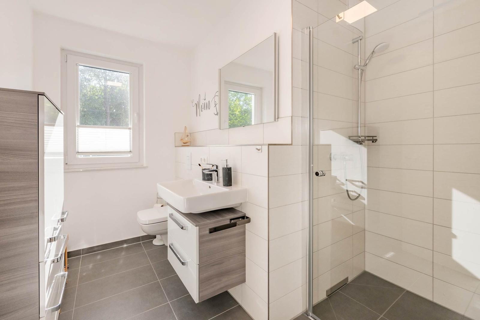 Badezimmer mit Dusche, Waschbecken und Toilette. Fenster mit Blick nach draußen.