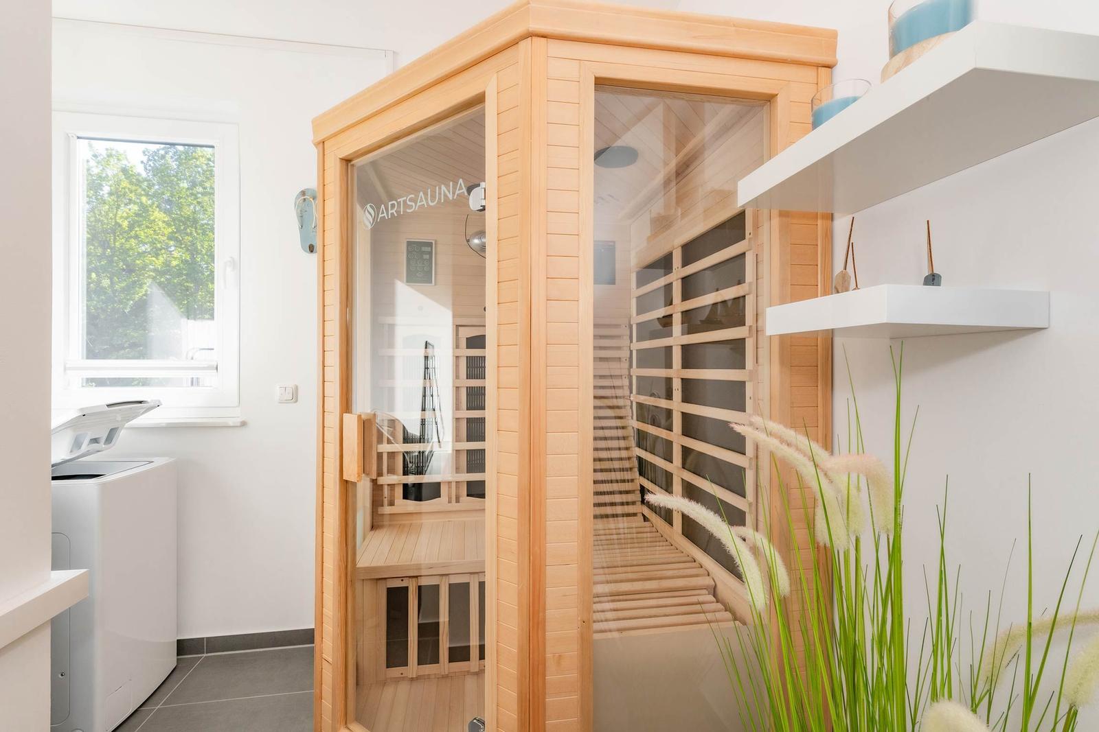 Eine Holzsauna mit Glasfront und Sitzbänken. Neben einem Fenster und einer Waschmaschine.