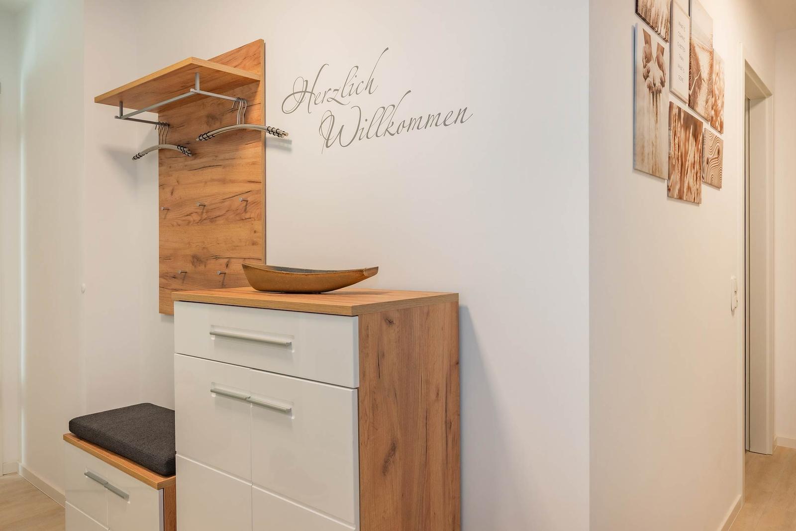 Eingangsbereich mit Holzgarderobe und Schminktisch. Wanddekoration mit Willkommensschild.