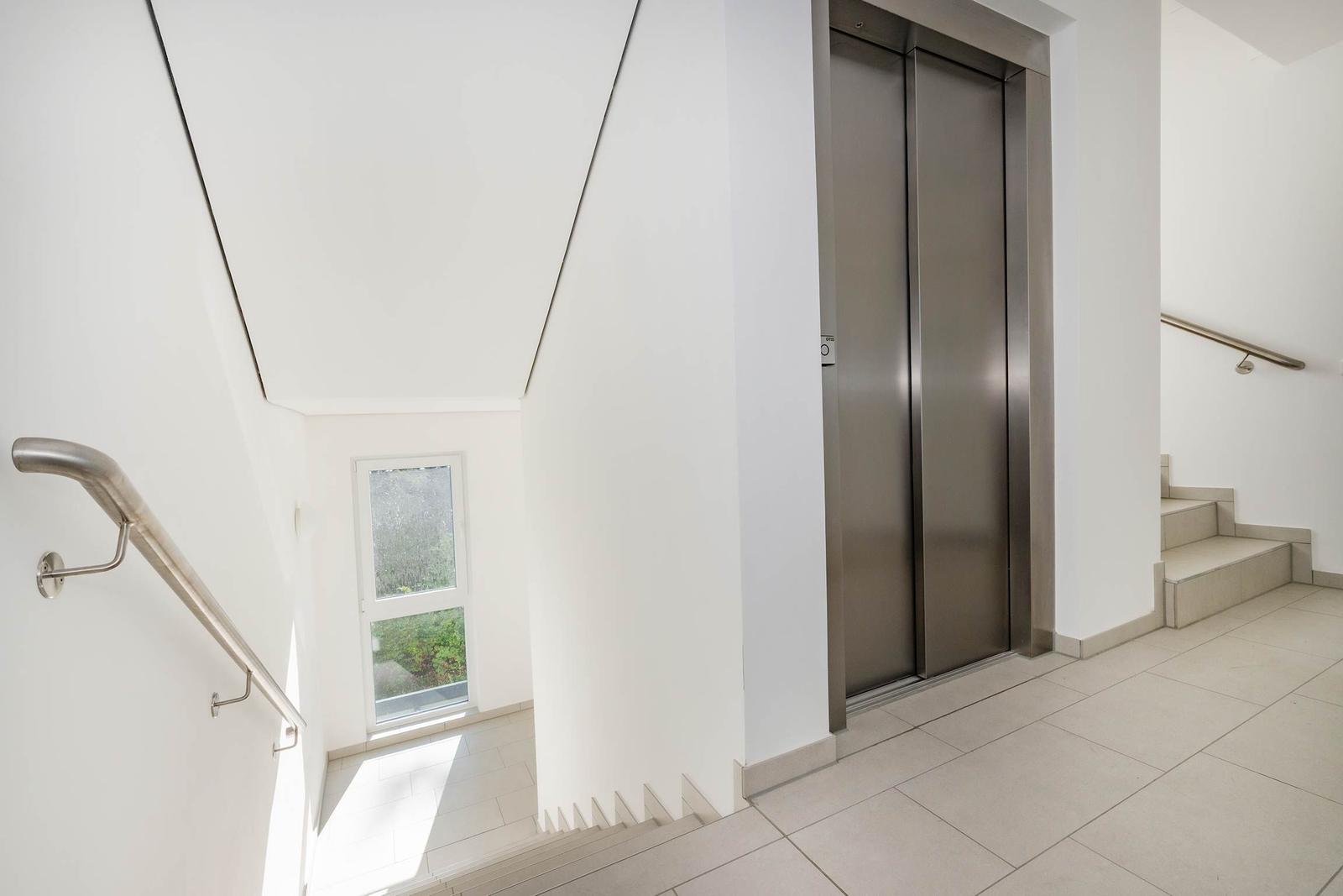 Haus mit Aufzug und Treppe. Fenster zeigt grüne Umgebung.