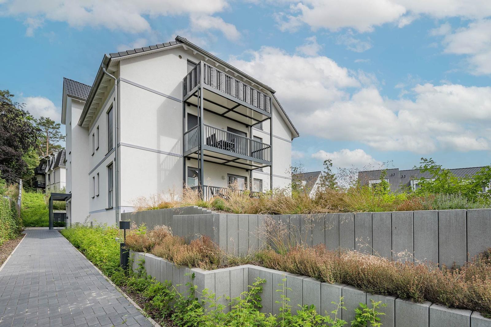 Modernes Mehrfamilienhaus mit Balkonen und gepflastertem Weg.