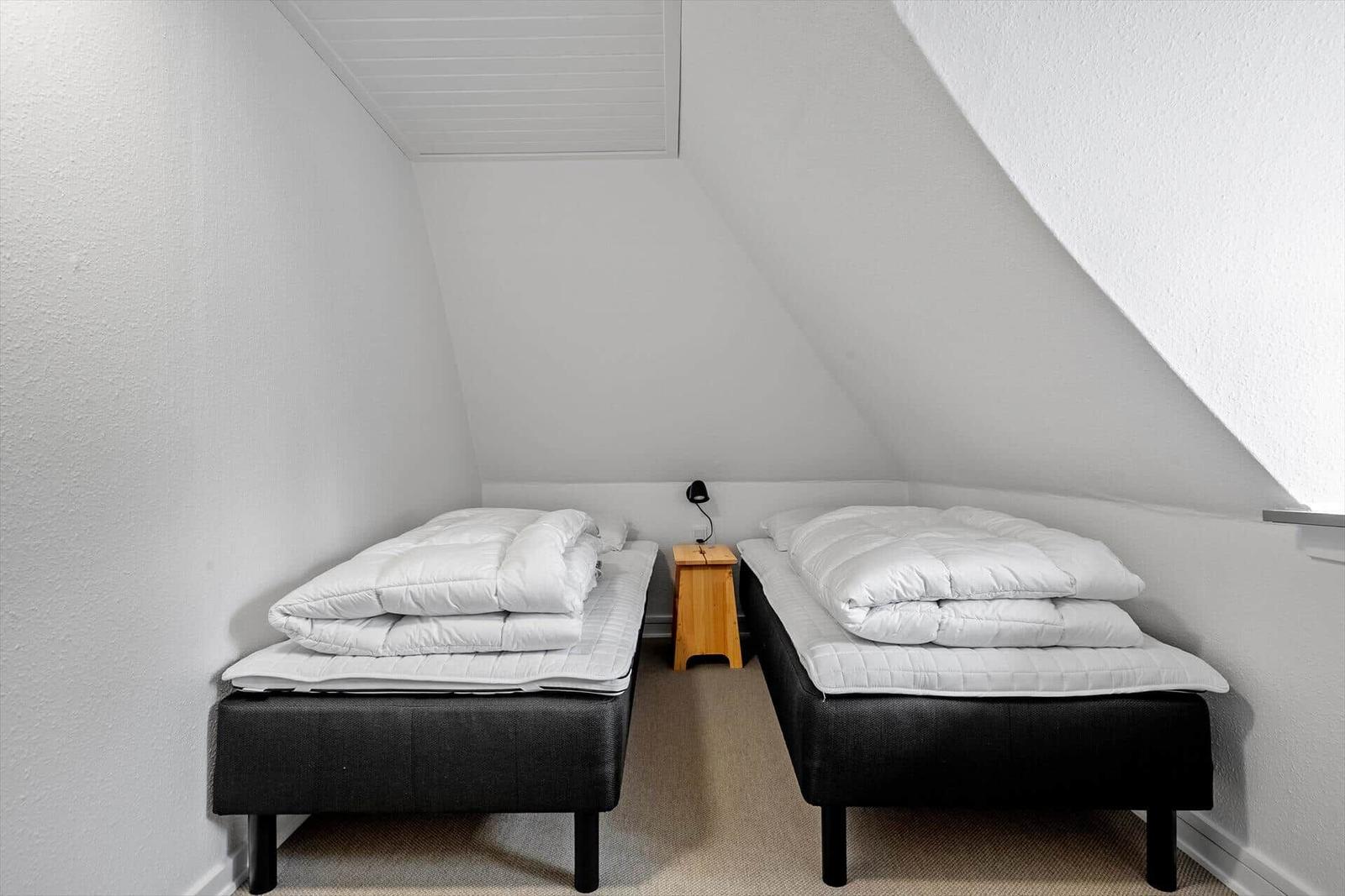 Zwei Matratzen mit weißen Decken in einem Dachzimmer mit schrägen Wänden und einem kleinen Nachttisch.