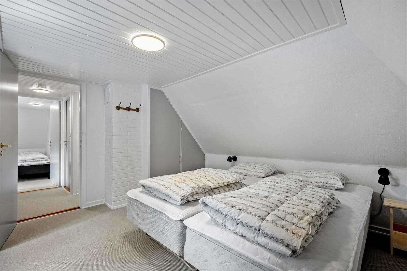 Schlafzimmer mit zwei Betten und Dachschrägen. Weiße Wände und Decke.