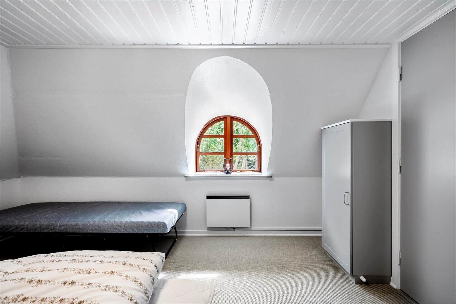 Zimmer mit Bett, Schrank und Bogenfenster mit Blick auf Grün.