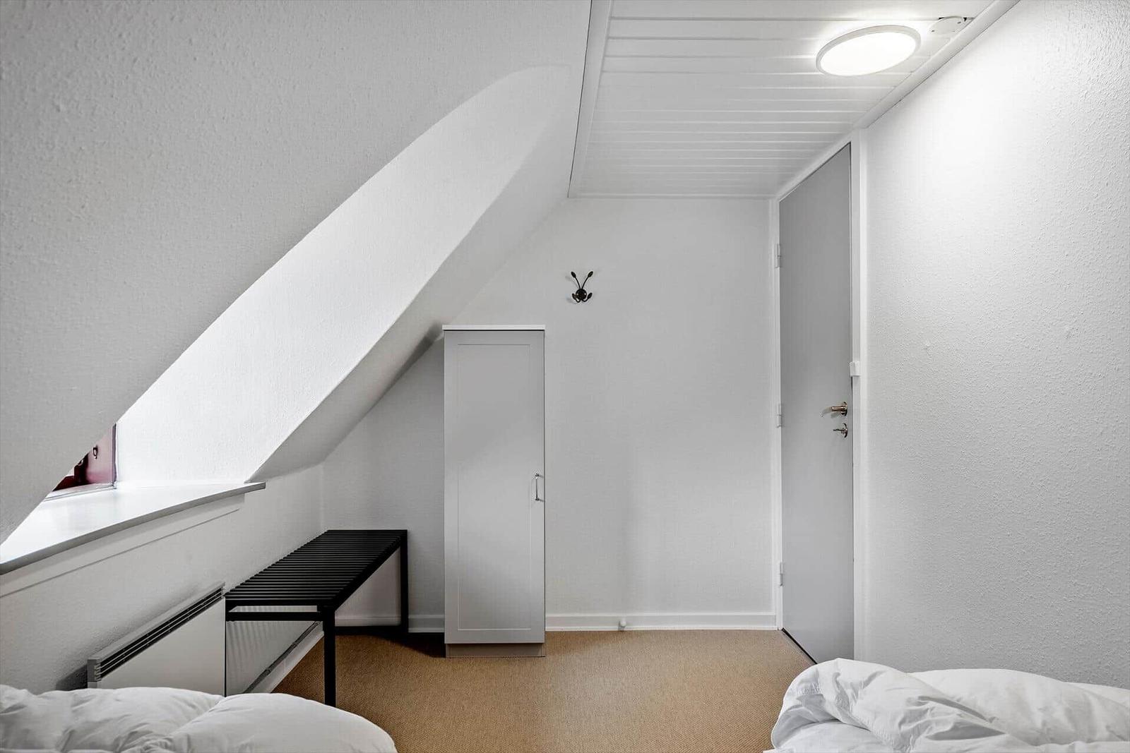 Zimmer mit schrägem Dach, Kleiderschrank, Bank und Bett.