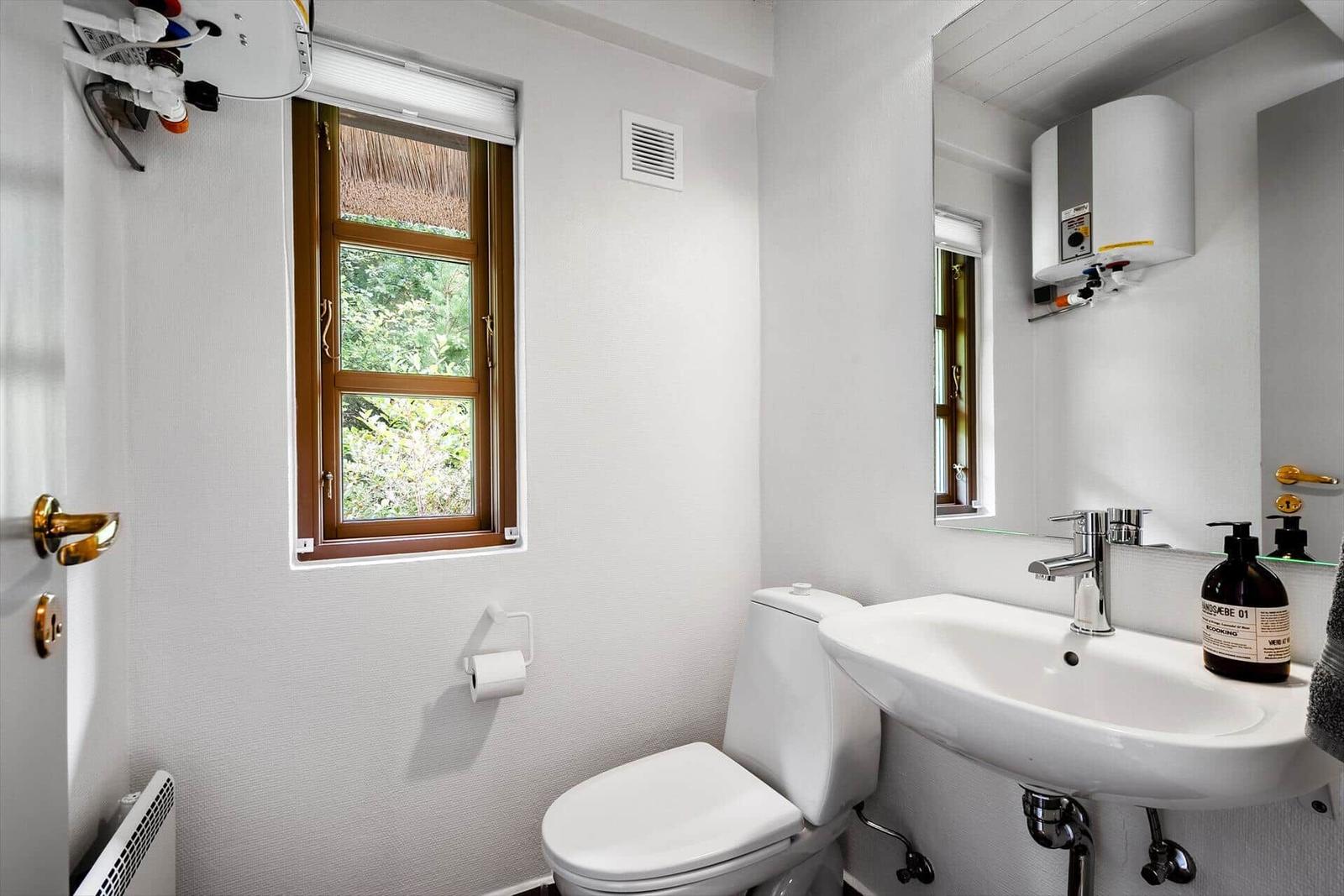 Badezimmer mit Toilette, Waschbecken und Fenster mit Blick auf Grün.