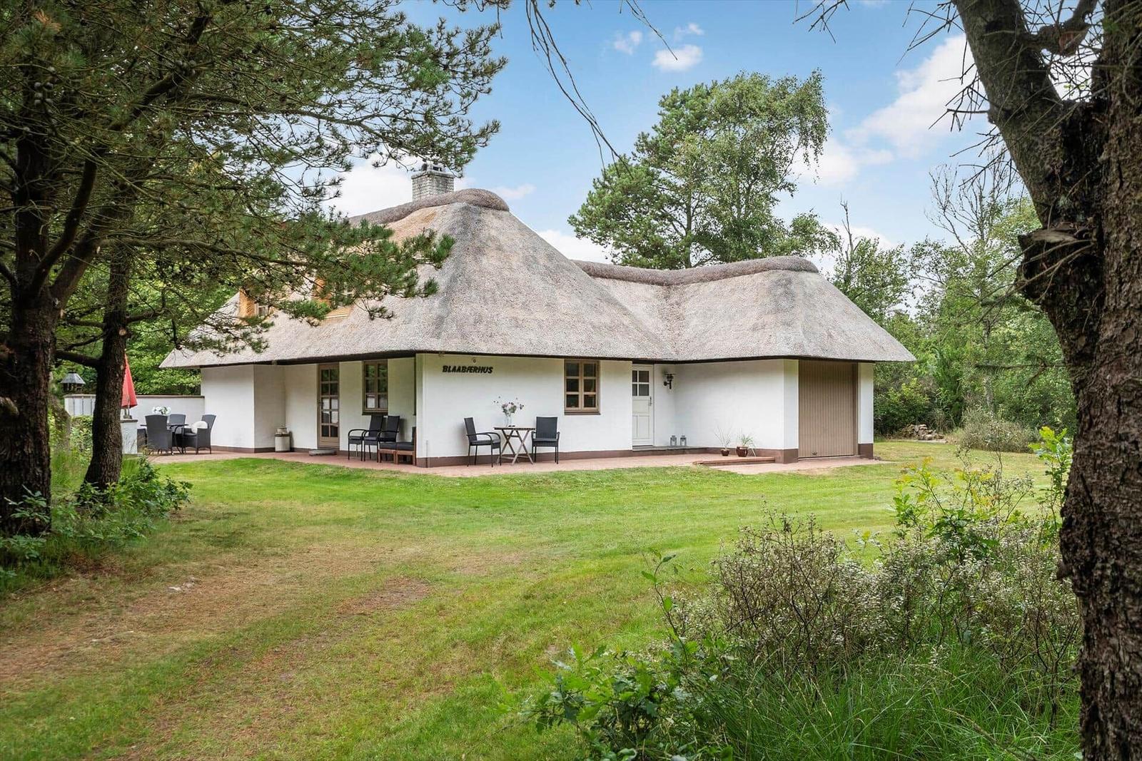 Haus mit Strohdach, Terrasse und Garten. Holzfenster und weiße Wände.