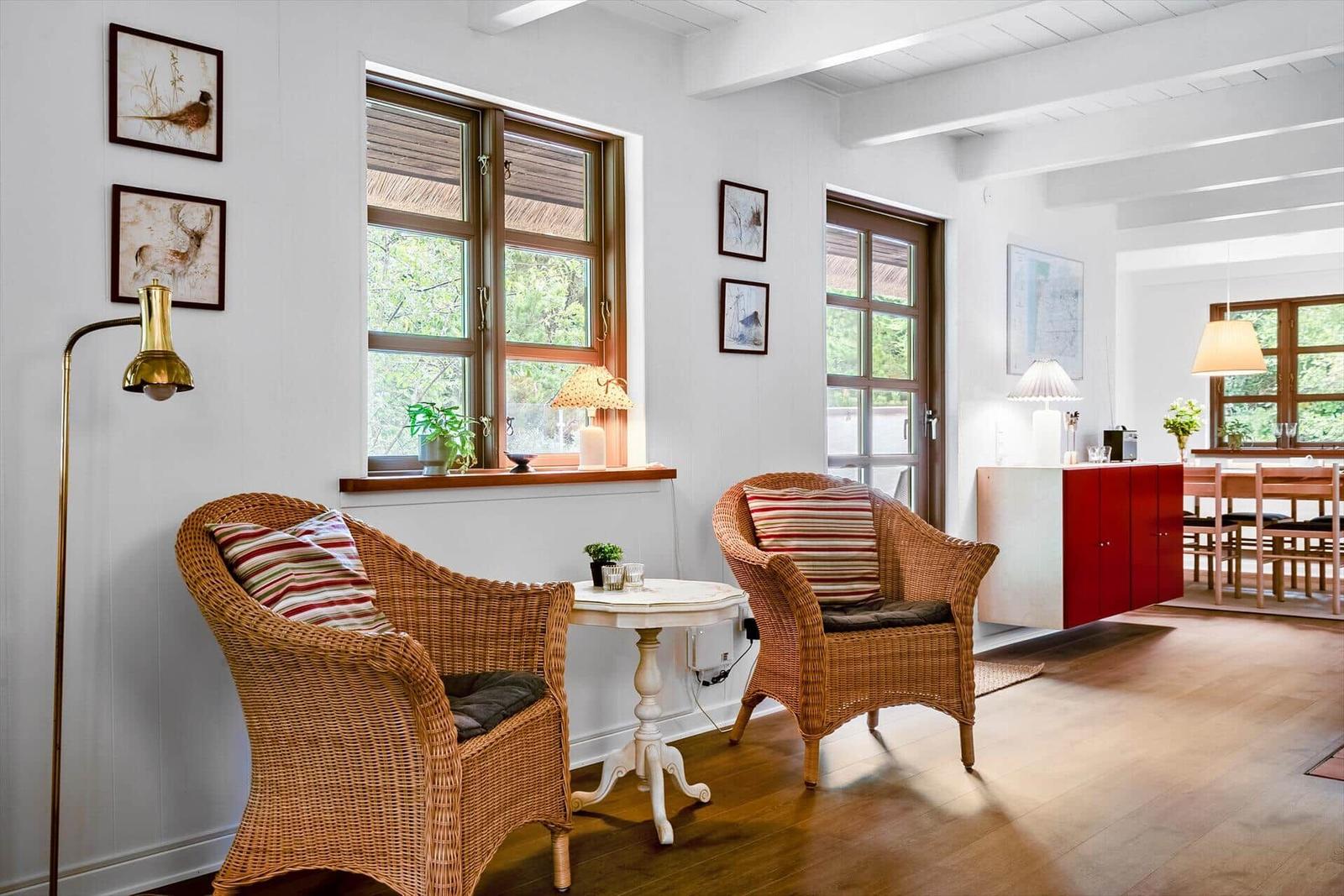 Zwei Rattan-Stühle stehen um einen weißen Tisch herum. Fenster und Türen blicken auf einen Garten.