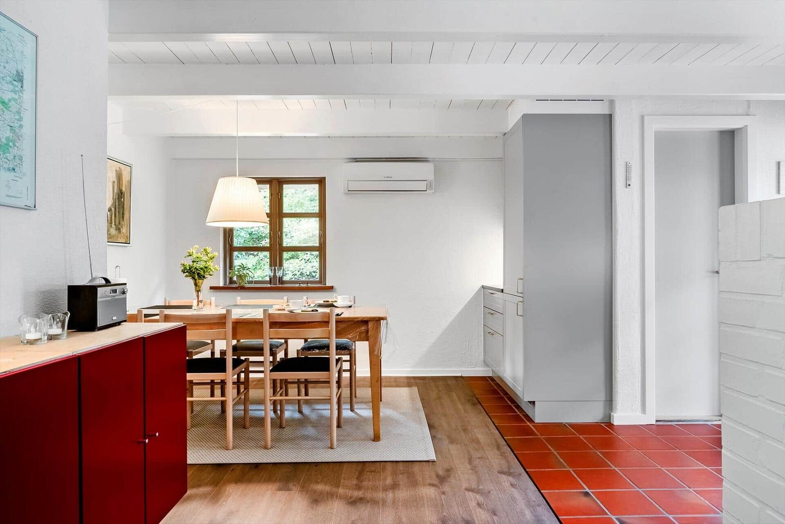 Esszimmer mit Holztisch, Stühlen und Fenster. Rote Fliesen und weiße Wände.