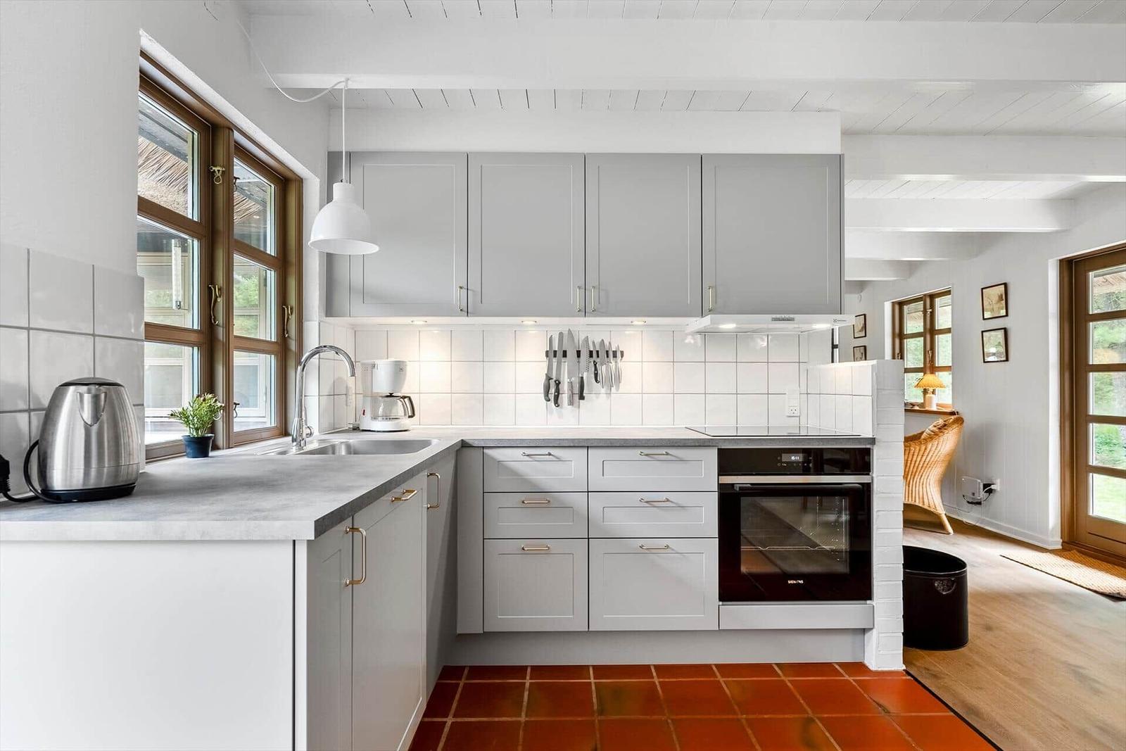 Küche mit grauen Schränken, weißer Arbeitsplatte und rotem Fliesenboden.