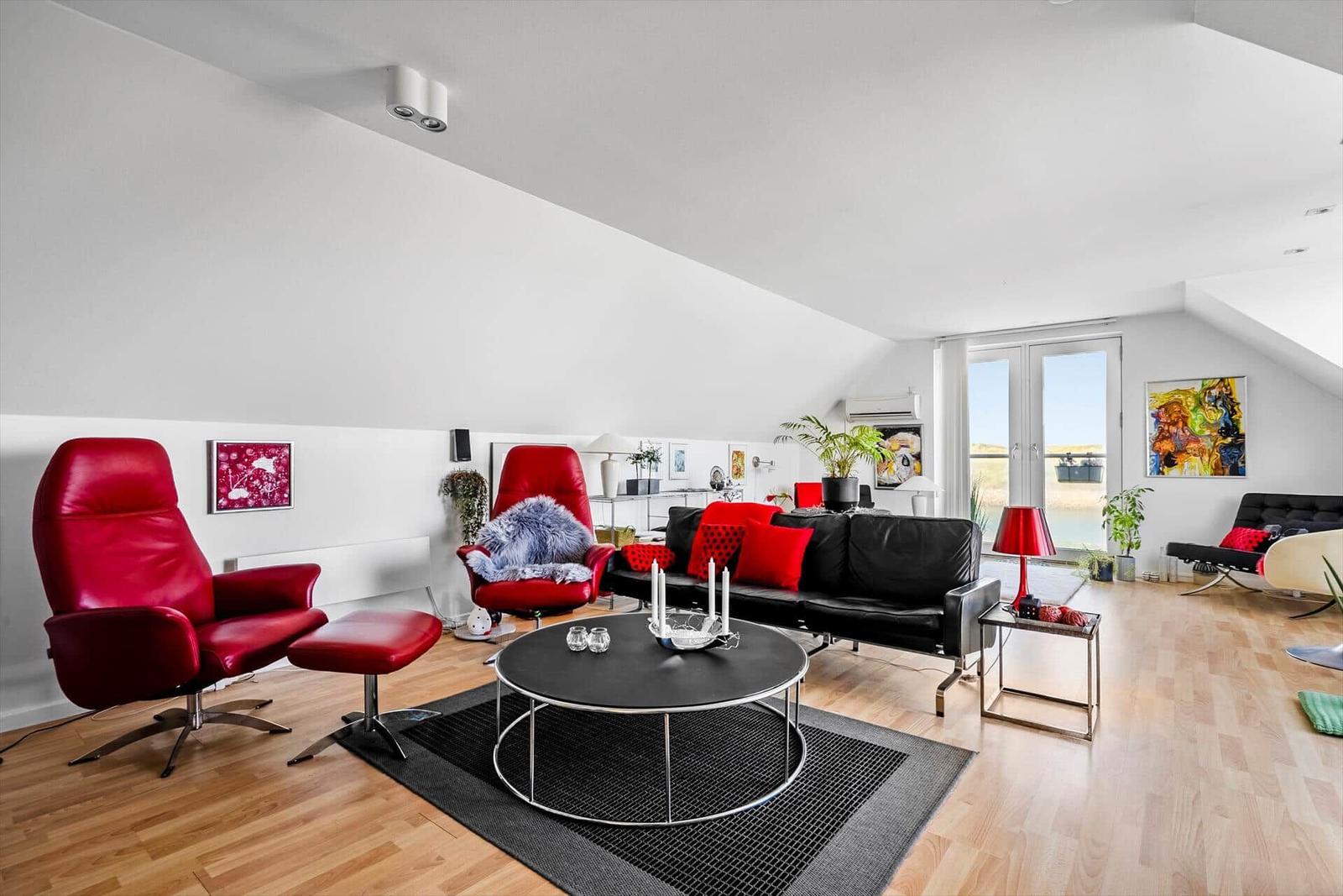 Wohnzimmer mit roten Sesseln, schwarzem Sofa und runden Tisch.