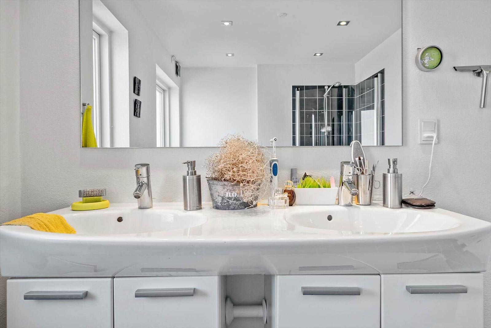 Doppelwaschbecken mit Spiegel, Dusche und Badzubehör.