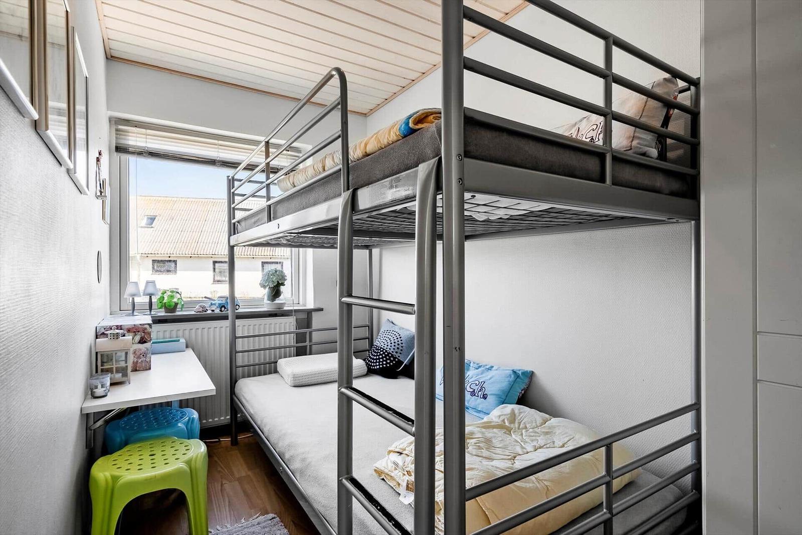 Zimmer mit Doppelstockbett, Fenster, Schreibtisch und Stühlen.