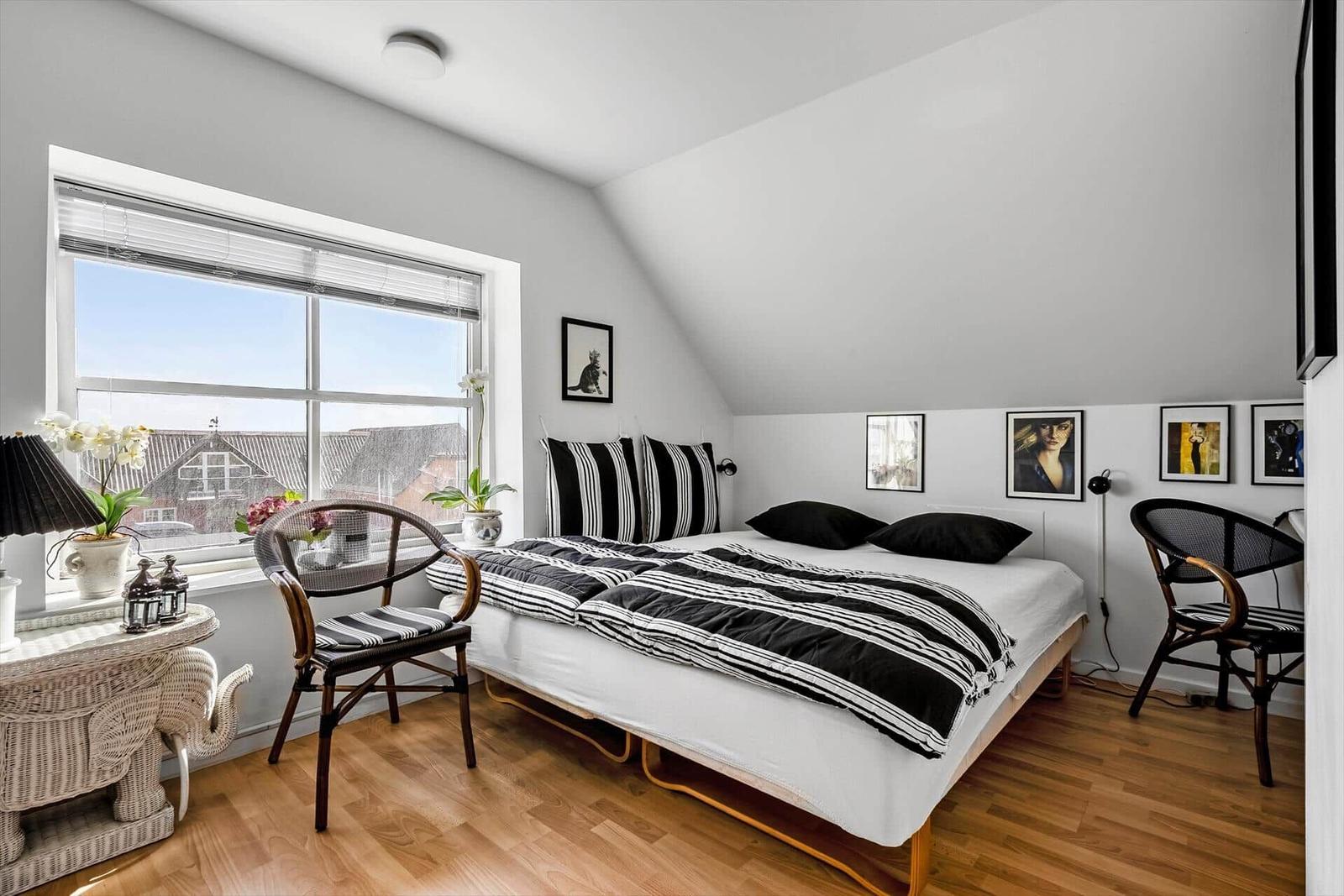 Schlafzimmer mit Doppelbett, Fenster, Stühlen und Wandbildern.