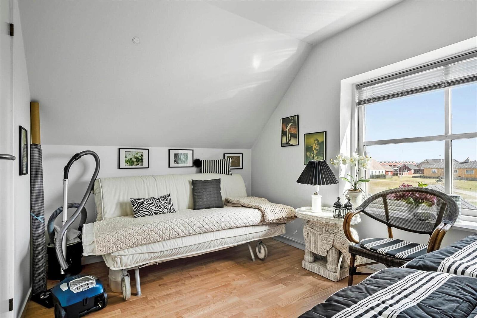 Zimmer mit Schlafcouch, Stuhl und Fensterblick auf Felder.