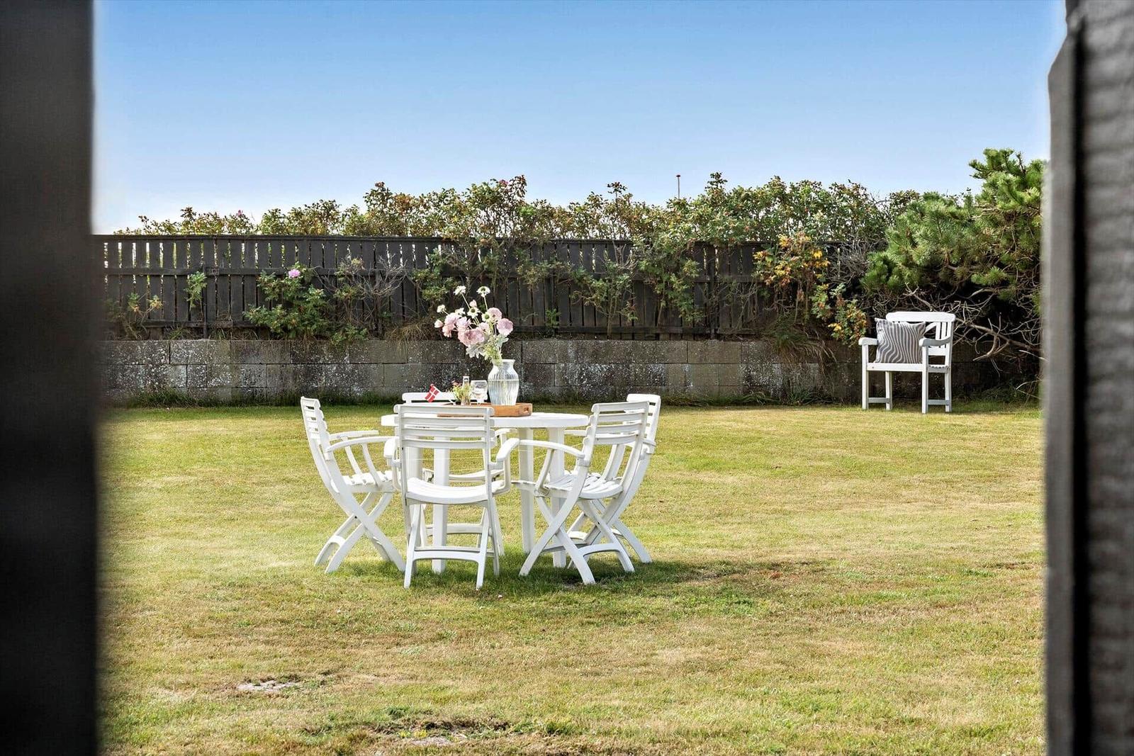 Hinterhof mit weißem Tisch und Stühlen, Blumen und Gartenmöbeln.