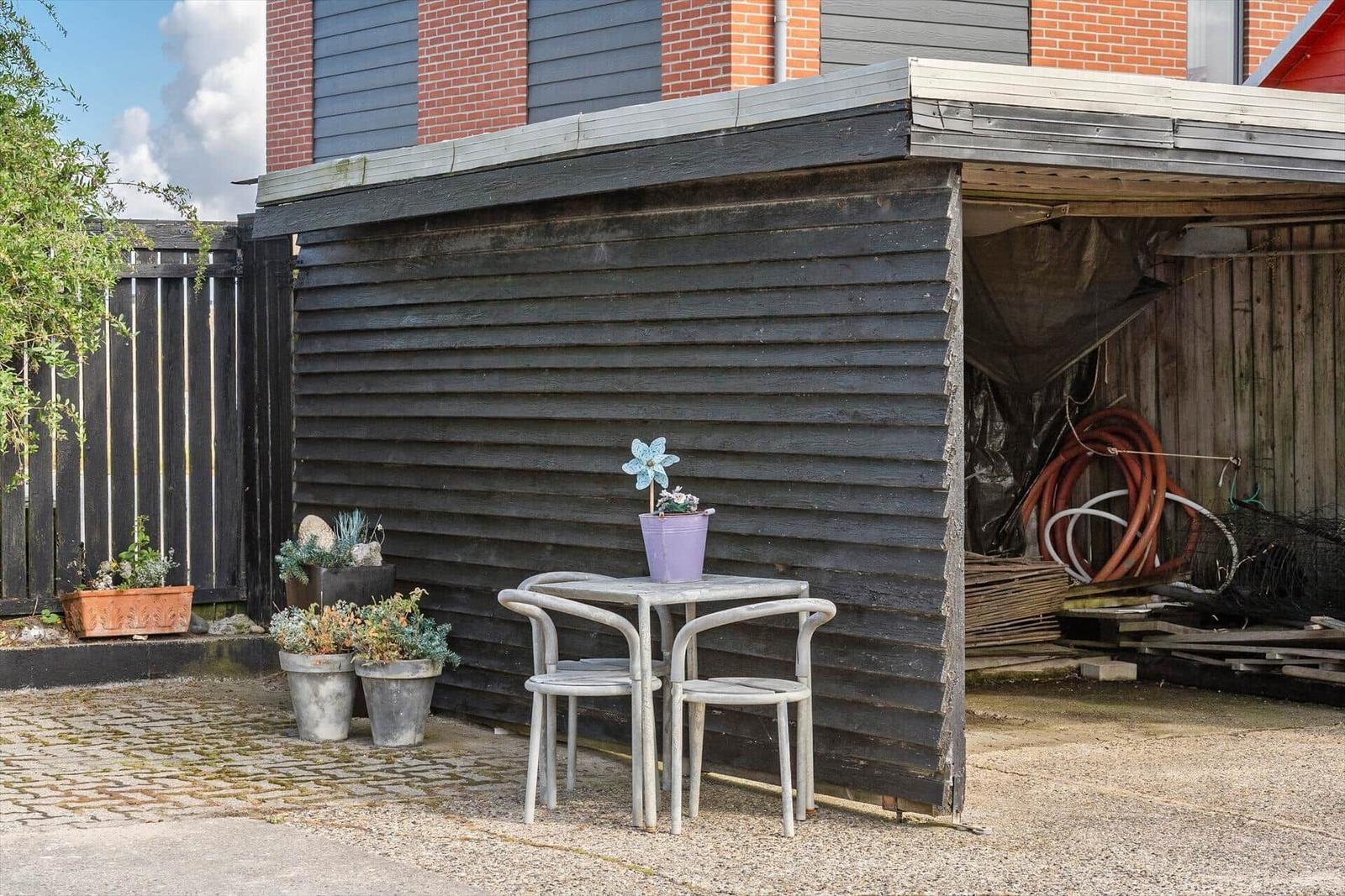 Außenbereich mit Tisch, zwei Stühlen und Pflanzen vor einem Holzschuppen.