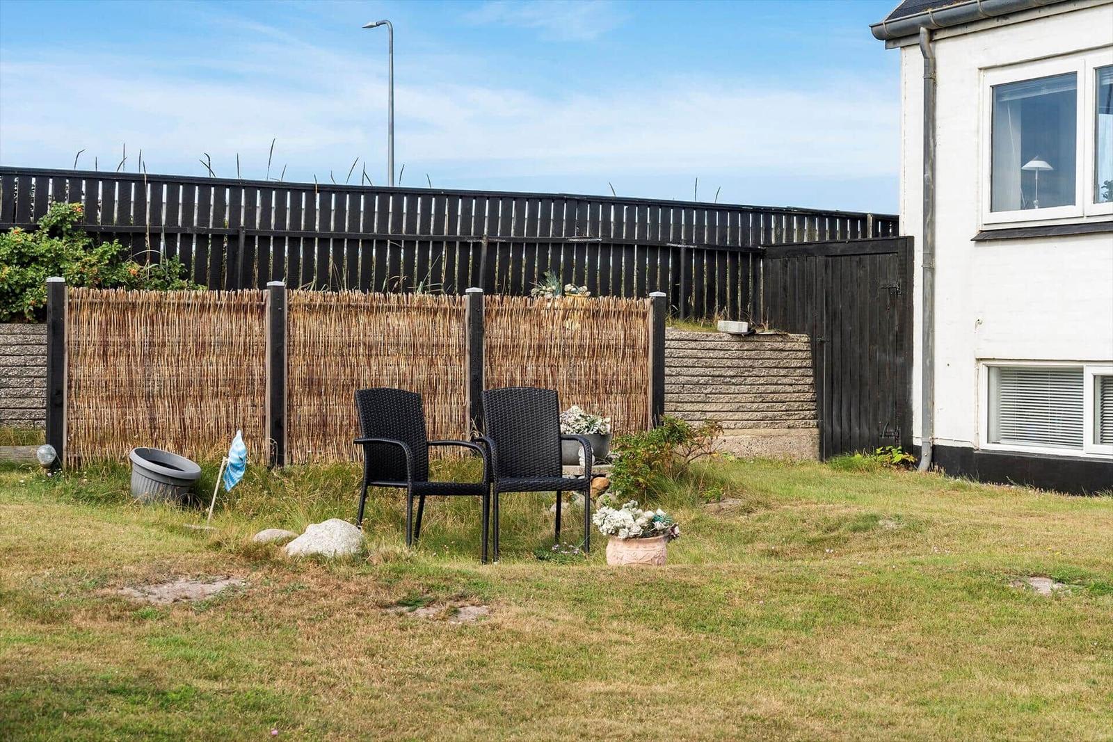 Hinterhof mit zwei schwarzen Stühlen, Zaun und Grasfläche.