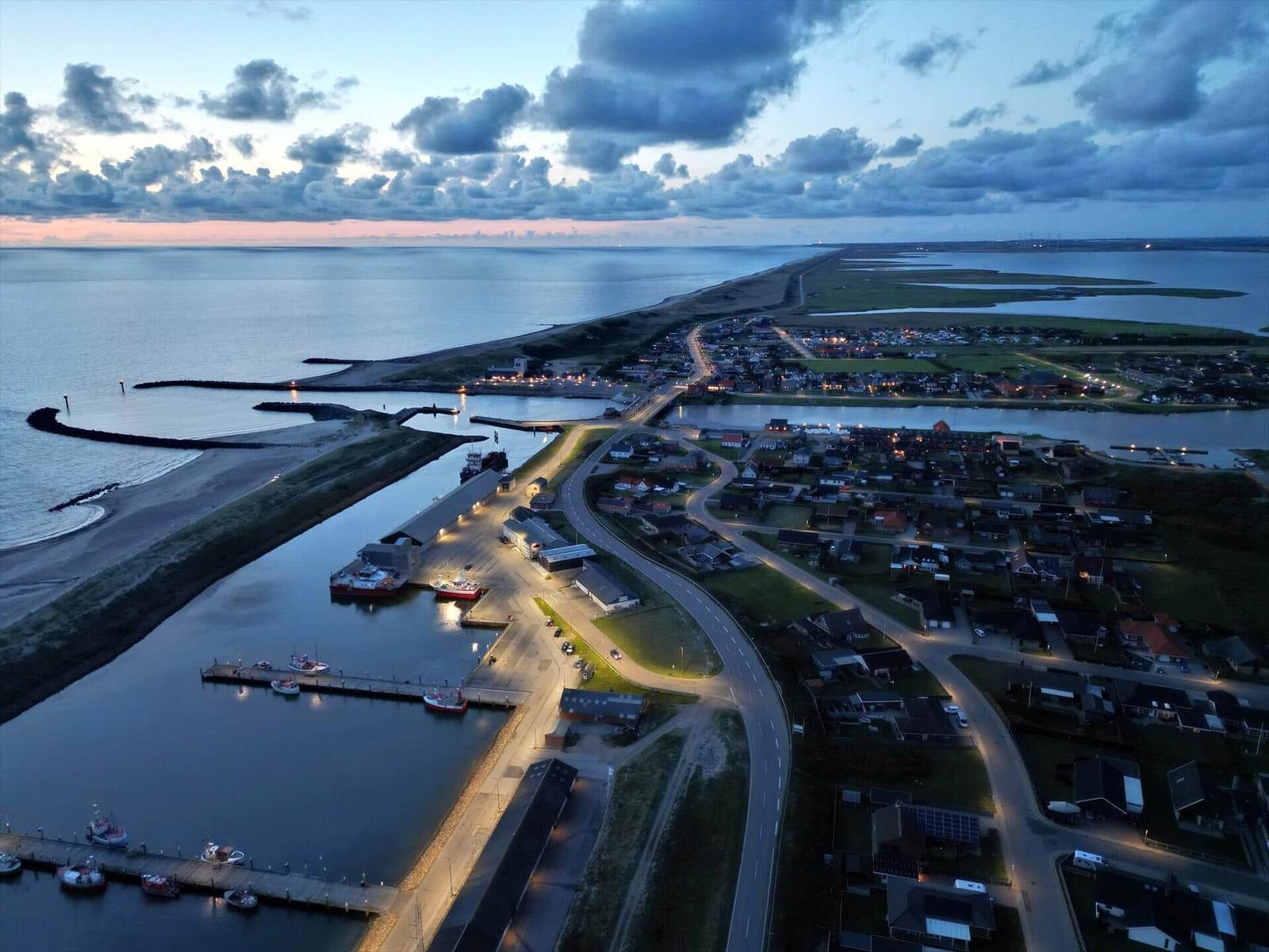 Aerial view of a coastal town at dusk with harbor, boats, and illuminated streets.